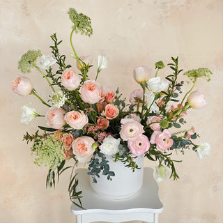 A very large floral arrangement filled with pastel pink, peach, and white flowers in a ceramic vase