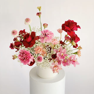 A large vibrant floral arrangement filled with bright pink, red, and white flowers in a ceramic vase