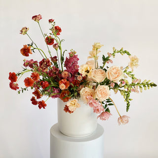 A very large floral arrangement filled with rust colored, light pink, and cream flowers in a ceramic vase