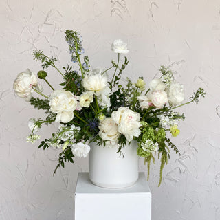 A very large floral arrangement filled with white flowers and greenery in a ceramic vase