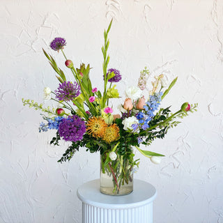 A tall floral arrangement full of vibrant purple, blue, yellow, and pink flowers