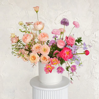 A very large floral arrangement filled with light peach, vibrant pink, and lavender flowers in a ceramic vase