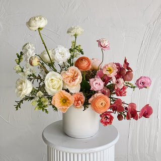 A very large floral arrangement with white, peach, pink, and maroon flowers in a ceramic vase