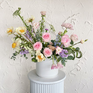 A very large floral arrangement filled with pastel pink, lavender, yellow and white flowers in a large ceramic vase