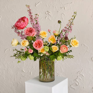 A large, tall floral arrangement with bright pink, yellow, green, and peachy flowers