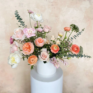 A large floral arrangement filled with light pink, peach, and white flowers in a ceramic vase