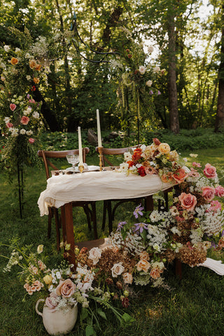 An outdoor garden wedding sweetheart table surrounded by big, summery flowers and a flower arch above it