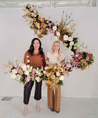 Two women standing behind a large asymmetrical hanging floral statement 